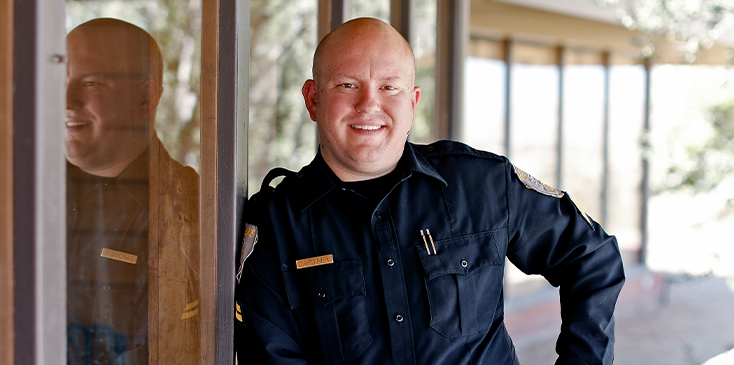bald man in a police uniform poses against a wall