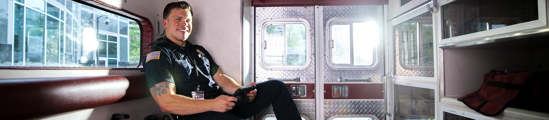 Jackson M. sits in the back of an ambulance. He is wearing a dark uniform and smiling.