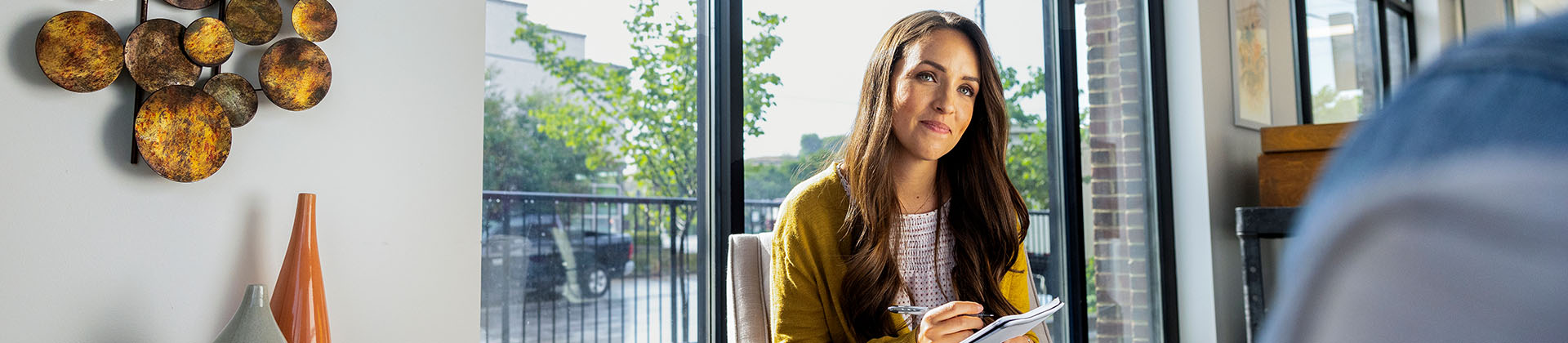 woman with a notepad and pen listens to someone out of frame