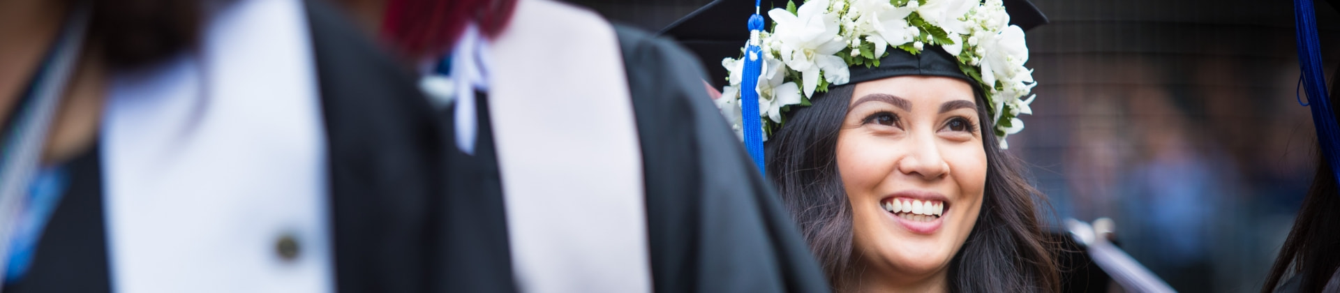  a line of college graduates, with  the focus on a woman wearing a cap decorated in white flowers