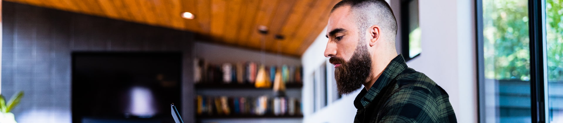 man with a beard works on a laptop in his home