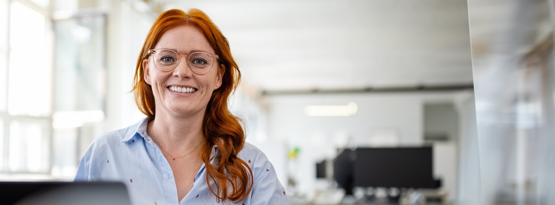 Woman with long red hair who wears glasses and a dress shirt