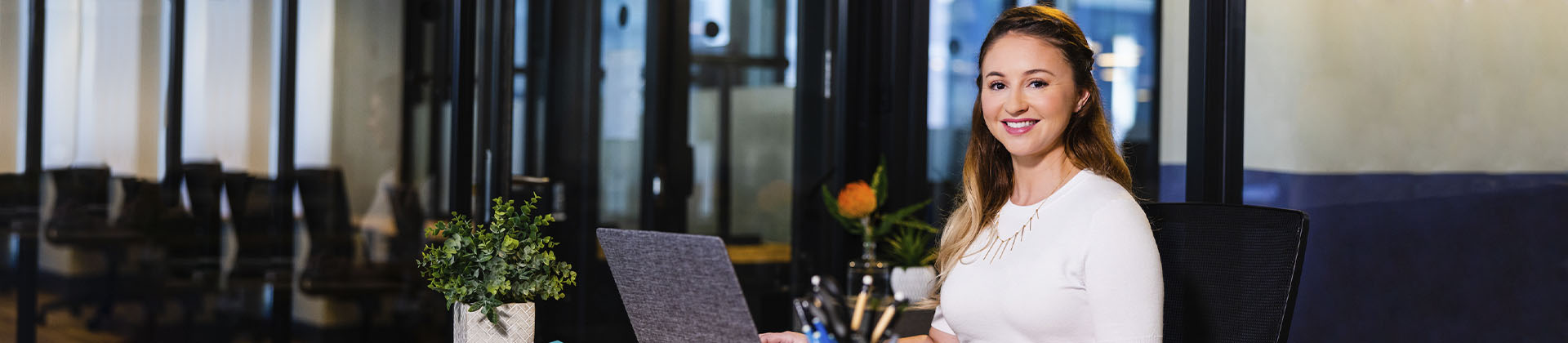 woman in office sitting at a desk with laptop open facing camera and smiling