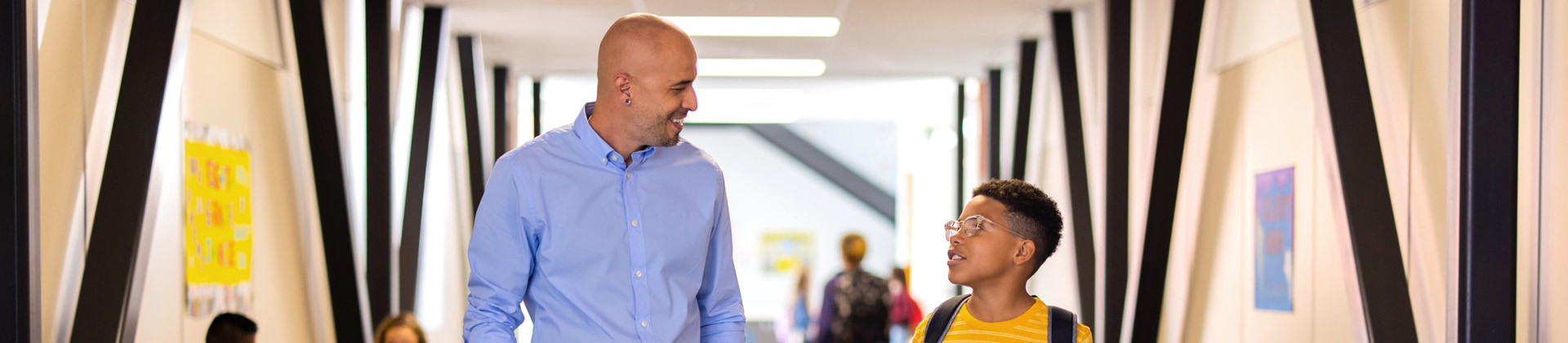 Man in a button-down shirt smiles at a young boy in glasses who also wears a backpack