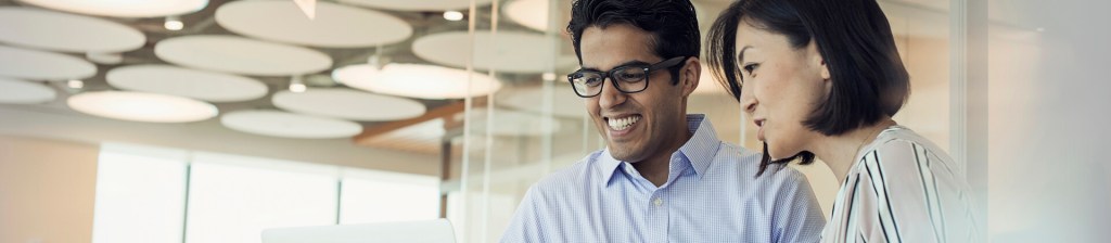 man and woman in office setting looking at computer with smiles