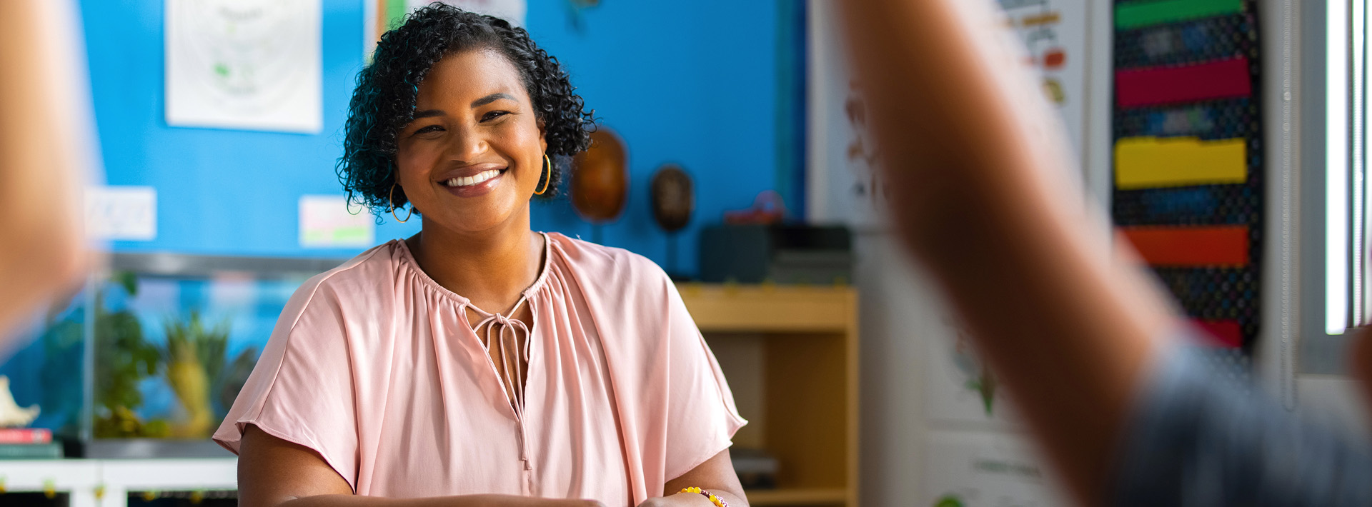 Woman with short curly hair and pink blouse teaches children in a classroom