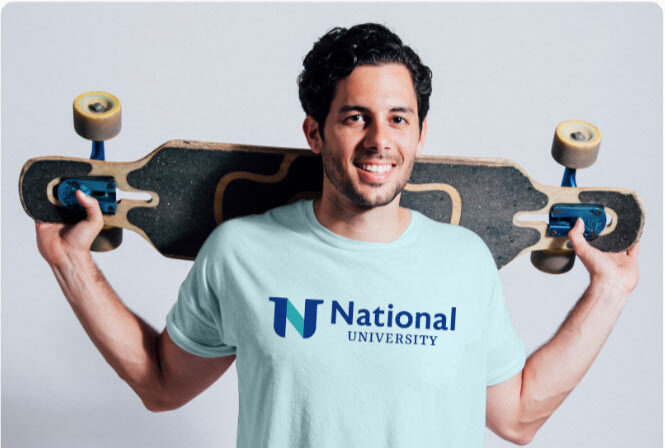 A man wearing a National University t-shirt holds a skateboard behind his back