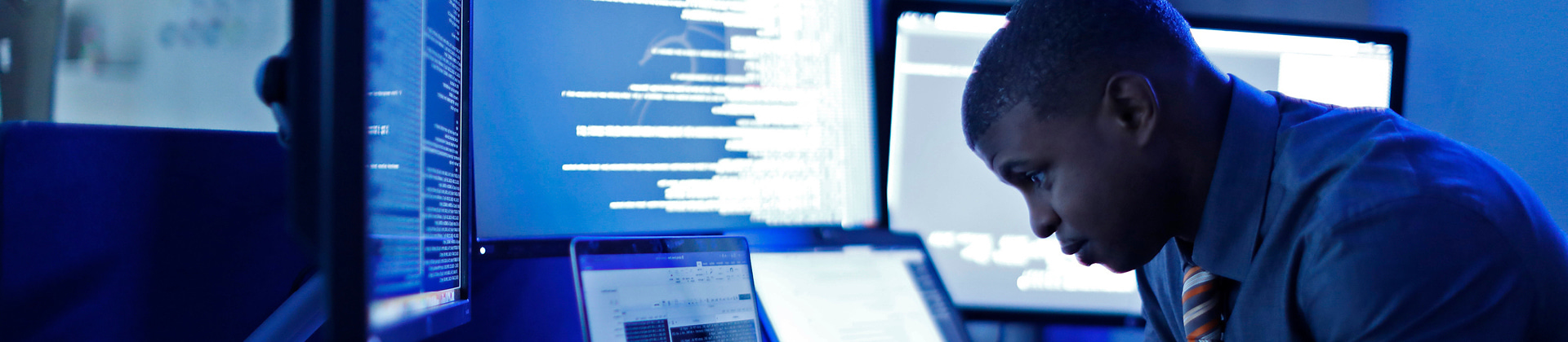 Person sitting at desk with multiple computer monitors with code on them