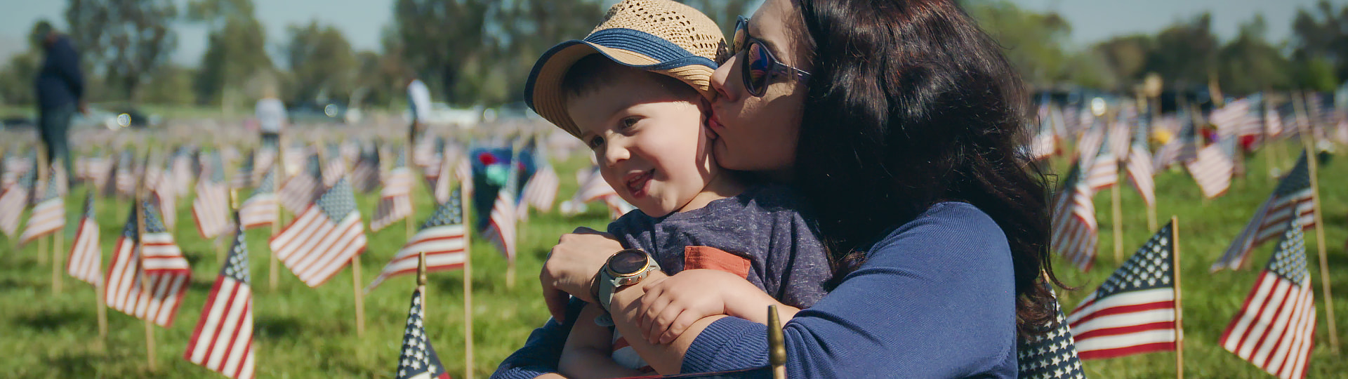 woman with a child stands in a field of American flags planted in the grass