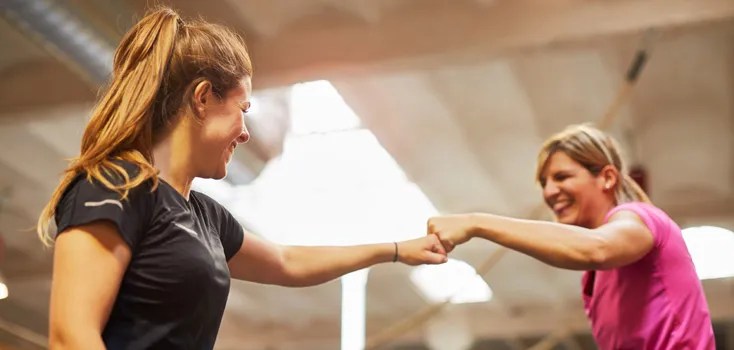 two women in gym fist bumping