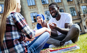 small group of people sitting in grass outside of building