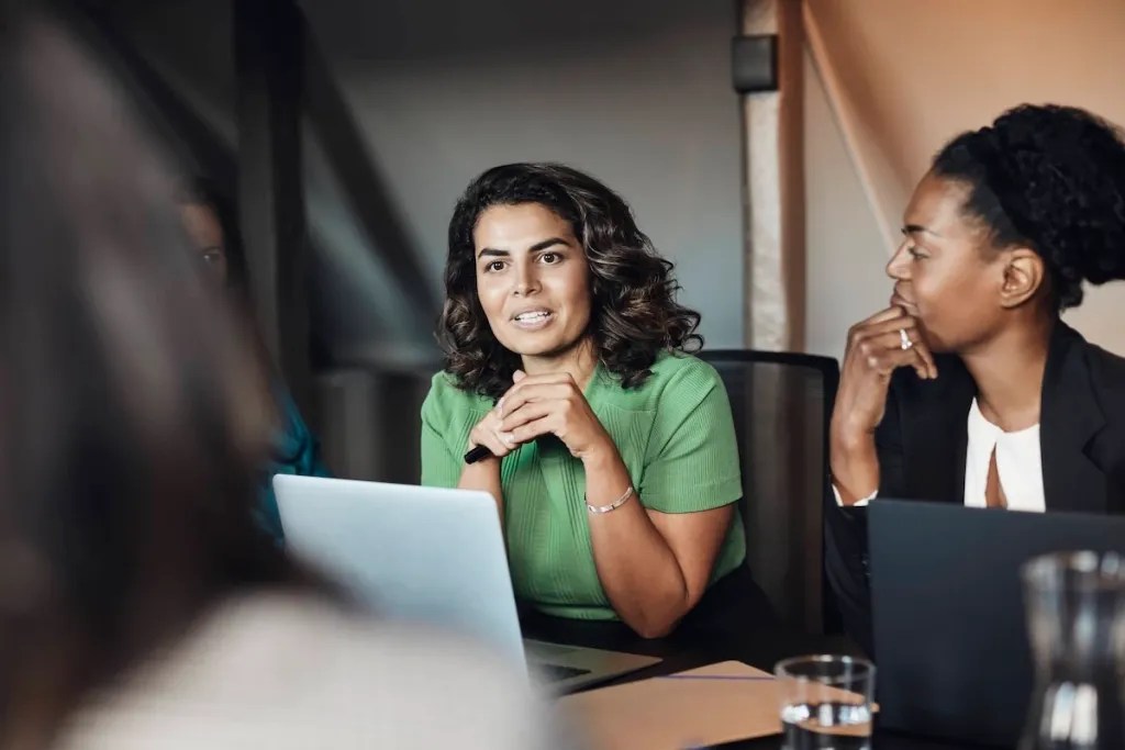 two women in a boardroom talking with someone across the table