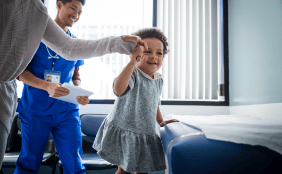 parent holding hand of child in hospital room with nurse