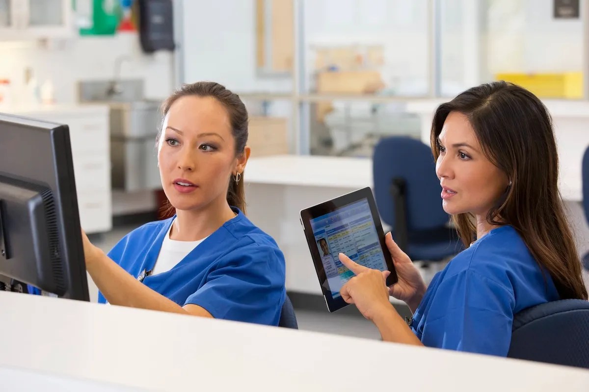 2 nurses wearing blue scrubs at computer